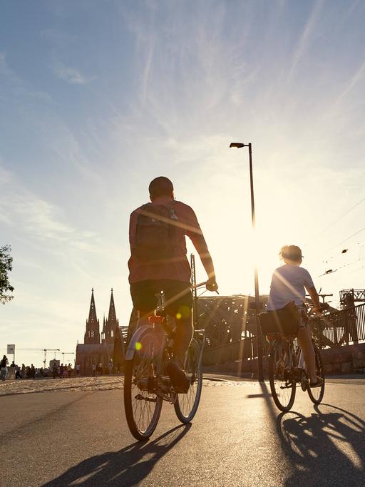 Zwei Fahrradfahrer radeln auf einer Straße in einer Stadt der Sonne entgegen.