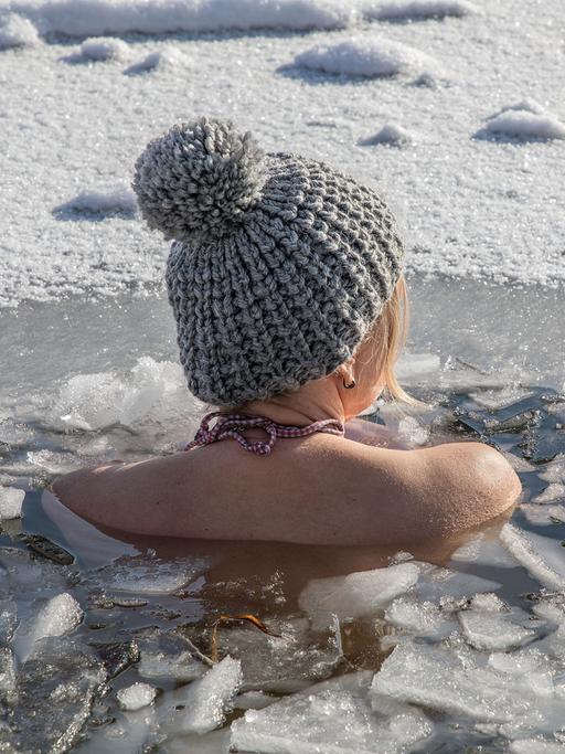 Eine Frau beim Eisbaden bei einer gefrorenen Wasserfläche im Winter, 2021.