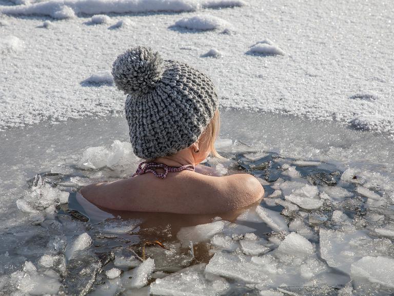 Eine Frau beim Eisbaden bei einer gefrorenen Wasserfläche im Winter, 2021.