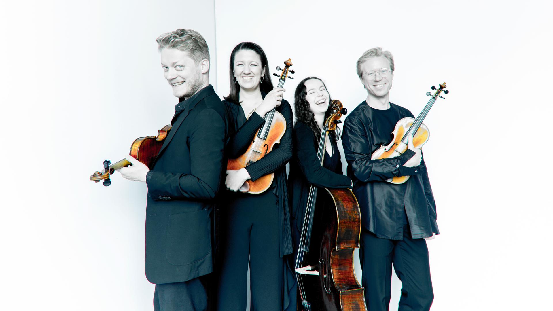 Zwei Musikerinnen und zwei Musiker stehen auf einer schwar-weiß-Fotografie dicht beieinander und halten ihre Instrumente, die bunt hervortreten. Zwei Musikerinnen und zwei Musiker stehen auf einer schwar-weiß-Fotografie dicht beieinander und halten ihre Instrumente, die bunt hervortreten.