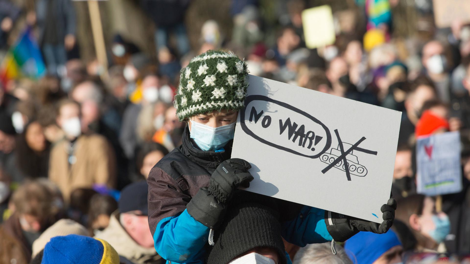 Ein Kind, getragen von einem Mann, hält ein Schild mit der Aufschrift "No War" in der Hand Ein Kind, getragen von einem Mann, hält ein Schild mit der Aufschrift "No War" in der Hand
