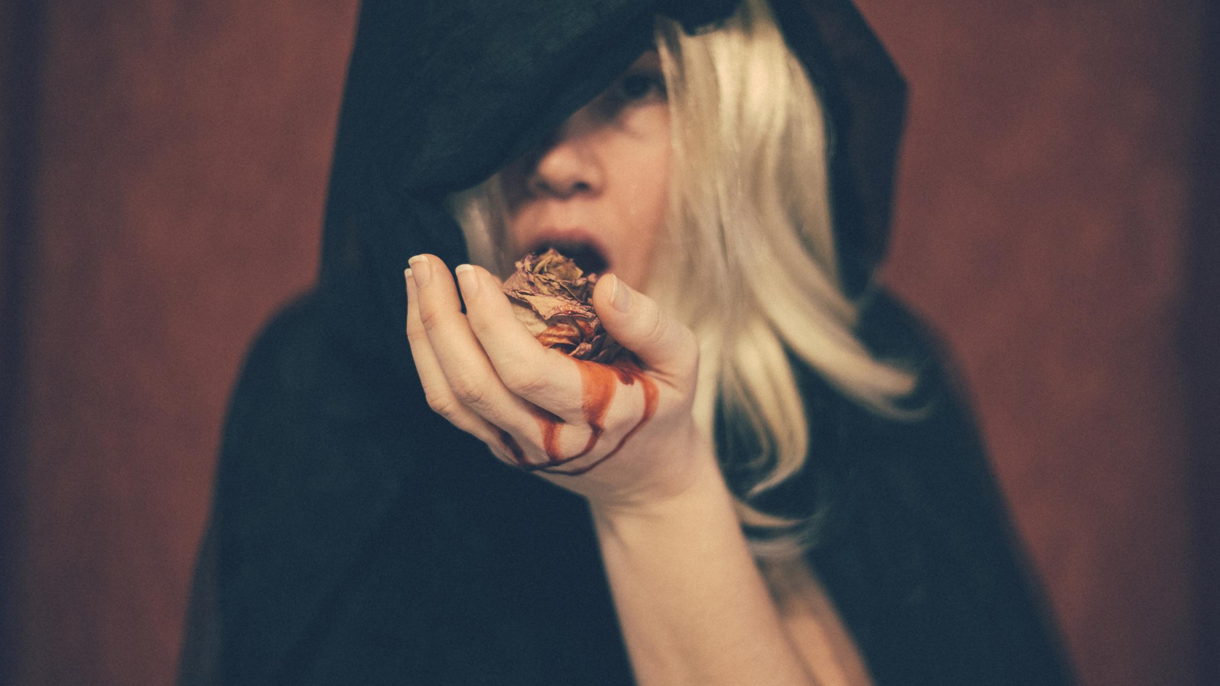 Frau im Kapuzenumhang hält in der blutigen Hand einen Frosch.