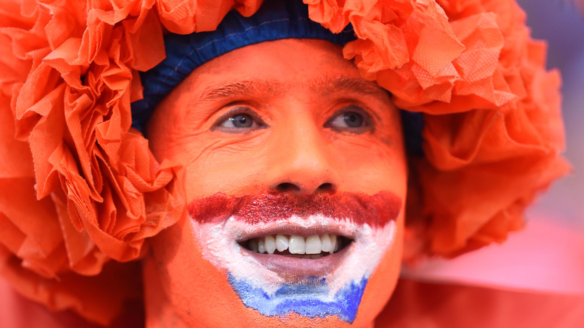 Ein Fan der niederländischen Fußballnationalmannschaft in einer Nahaufnahme. Das Gesicht des Mannes ist komplett orange bemalt, außerdem trägt er eine orangefarbene Perücke. Ein Fan der niederländischen Fußballnationalmannschaft in einer Nahaufnahme. Das Gesicht des Mannes ist komplett orange bemalt, außerdem trägt er eine orangefarbene Perücke.