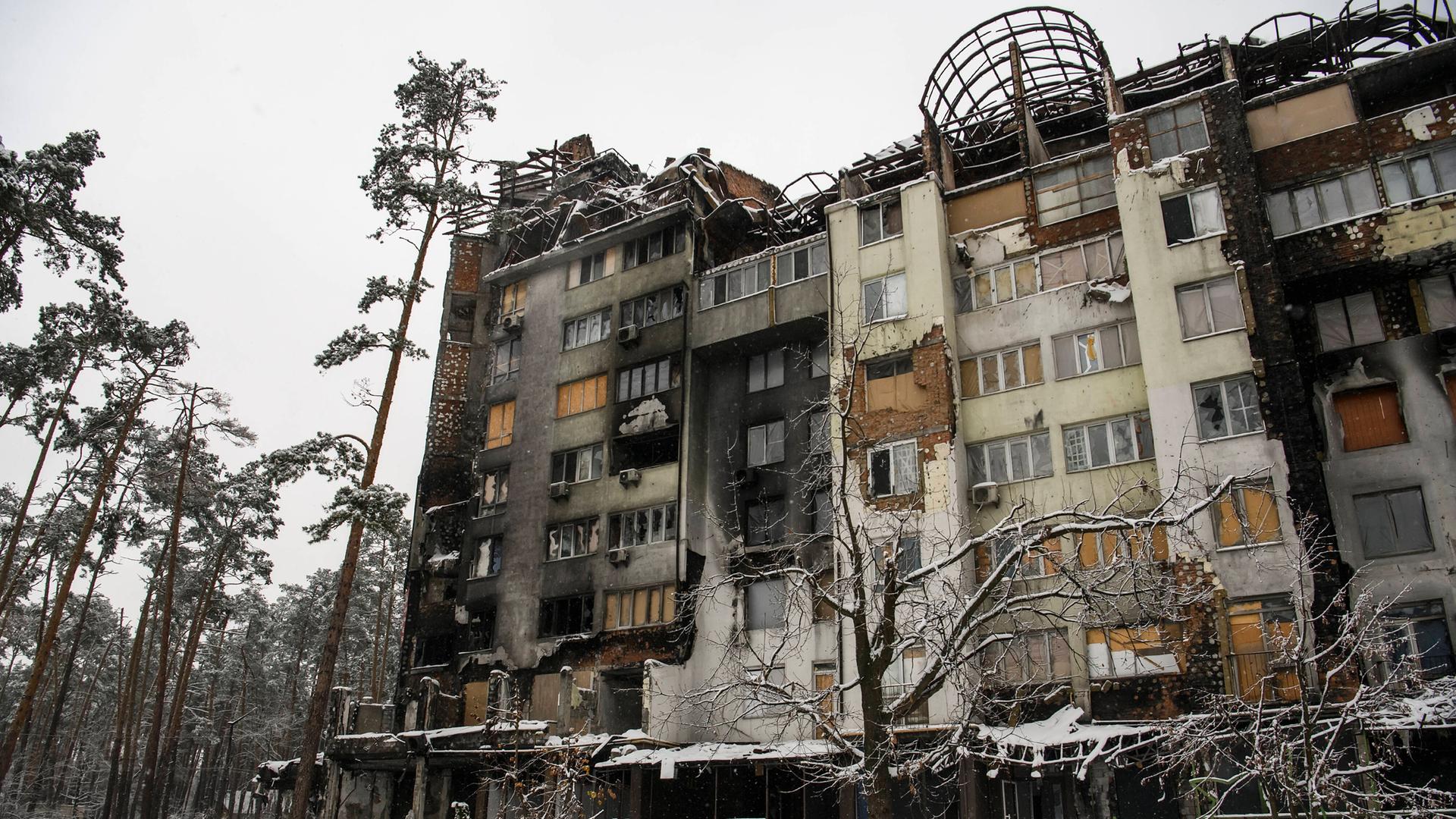 Ein Schneedecke bedeckt die Straße vor einem zerstörten Apartment-Haus in der ukrainische Stadt Irpin