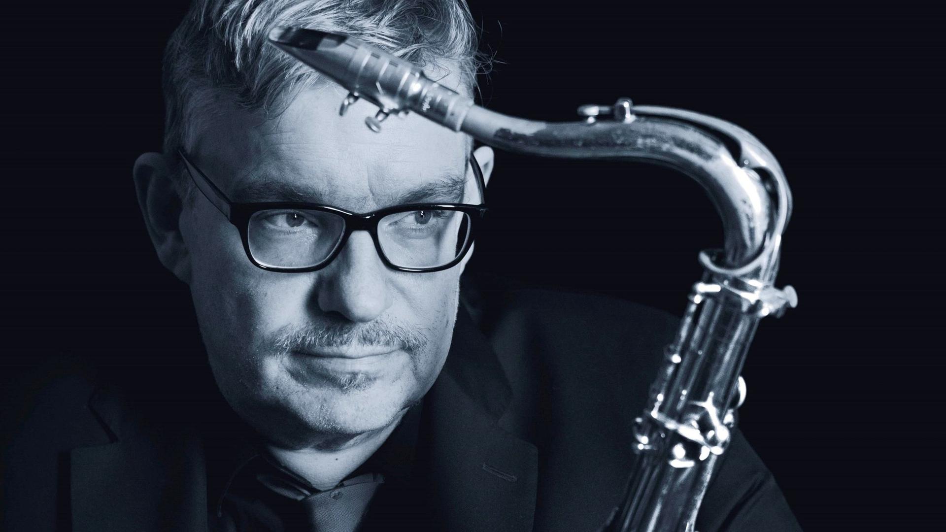 Ein Mann mit Brille und kurzem Haar umarmt sein Saxophon. Ein Mann mit Brille und kurzem Haar umarmt sein Saxophon.