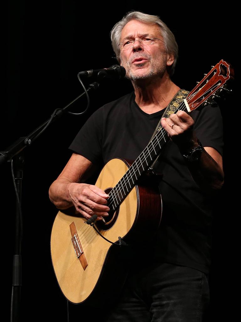 Liedermacher Reinhard Mey steht mit seiner Gitarre auf einer Bühne. Der Hintergrund hinter ihm ist ganz schwarz.
