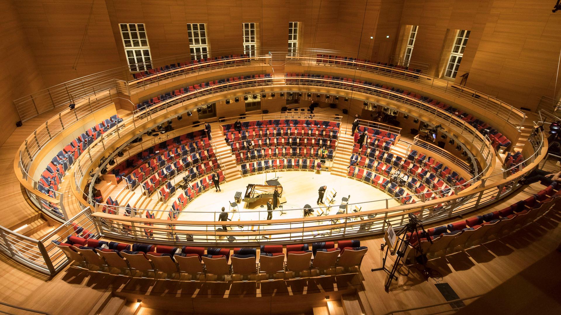 Blick in den halbrunden Saal mit rot-blauen Sitzreihen und extrem hoher Decke. Blick in den halbrunden Saal mit rot-blauen Sitzreihen und extrem hoher Decke.