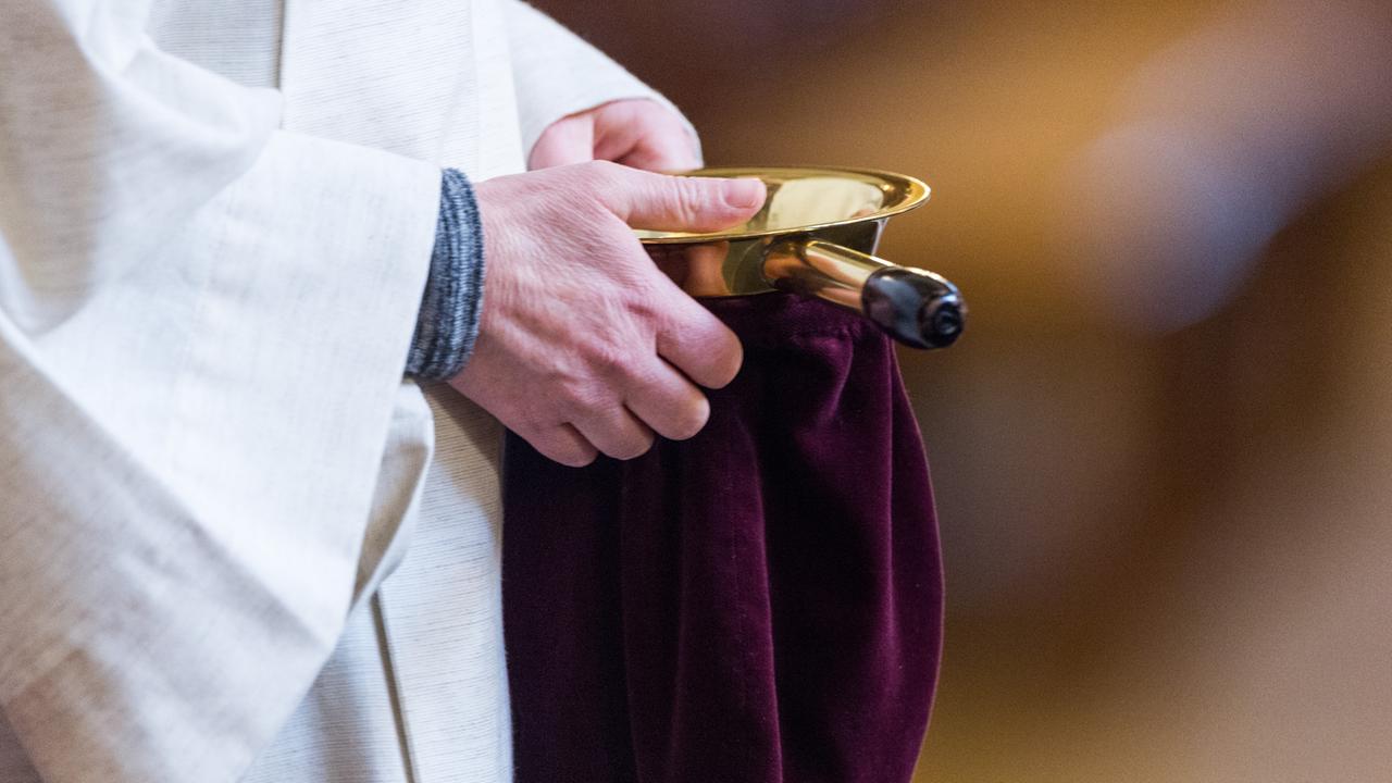 Eine Messdienerin hält im Berliner Dom einen Klingelbeutel.