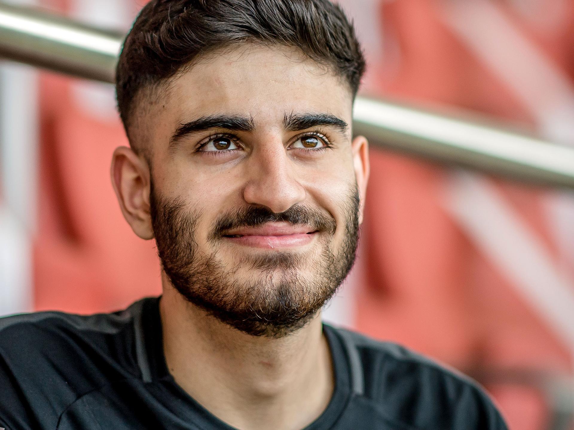 Der E-Sportler Umut Gültekin sitzt in einem leeren Stadion und blickt lächelnd in die Kamera.