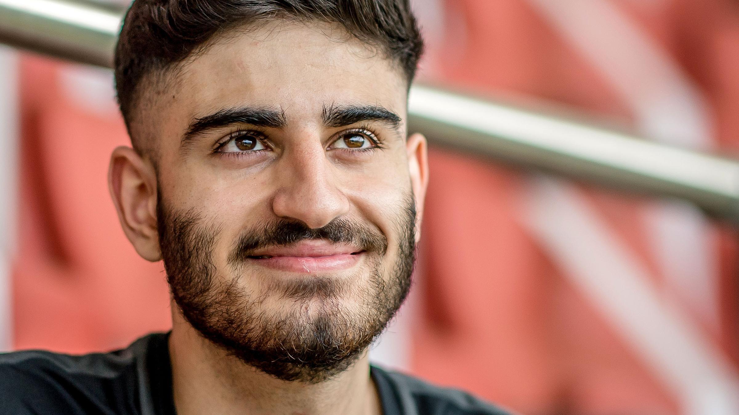 Der junge E-Sportler Umut Gültekin sitzt in einem leeren Stadion und blickt lächelnd in die Kamera.