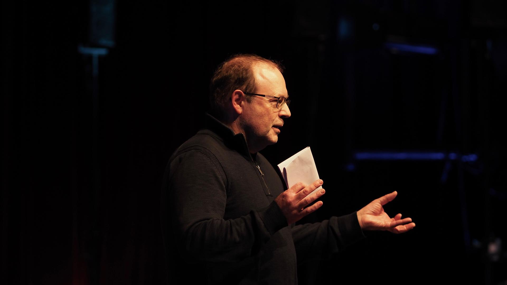Der Komponist Jörg Mainka steht im Scheinwerferlicht auf einer dunklen Bühne