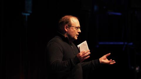 Der Komponist Jörg Mainka steht im Scheinwerferlicht auf einer dunklen Bühne