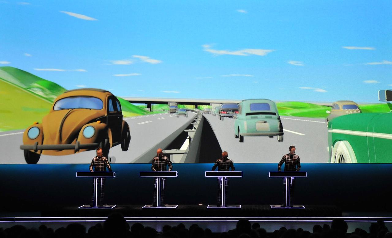Kraftwerk beim Live-Auftritt zu Ihrer Retrospektive in der Londoner Tate Modern. Im Hintergrund ist eine Visualisierung der deutschen Autobahn mit VW Käfer zu sehen.