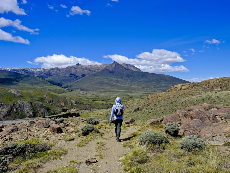Eine Backpackerin im blauen Anorak wandert durch die Berge in Patagonien, Argentinien.
