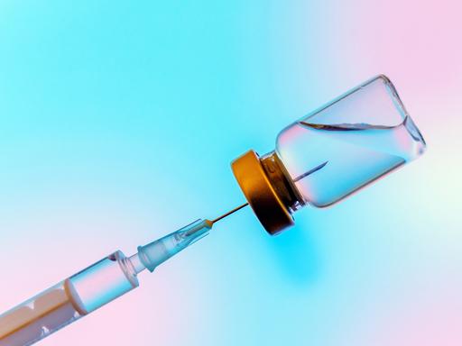 Studioaufnahme einer Spritze, die Flüssigkeit, einen Impfstoff, aus einem Gefäß zieht.