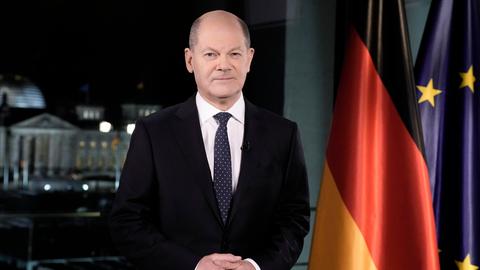 Bundeskanzler Olaf Scholz steht während seiner Neujahrsansprache vor den Flaggen Deutschlands und der EU.