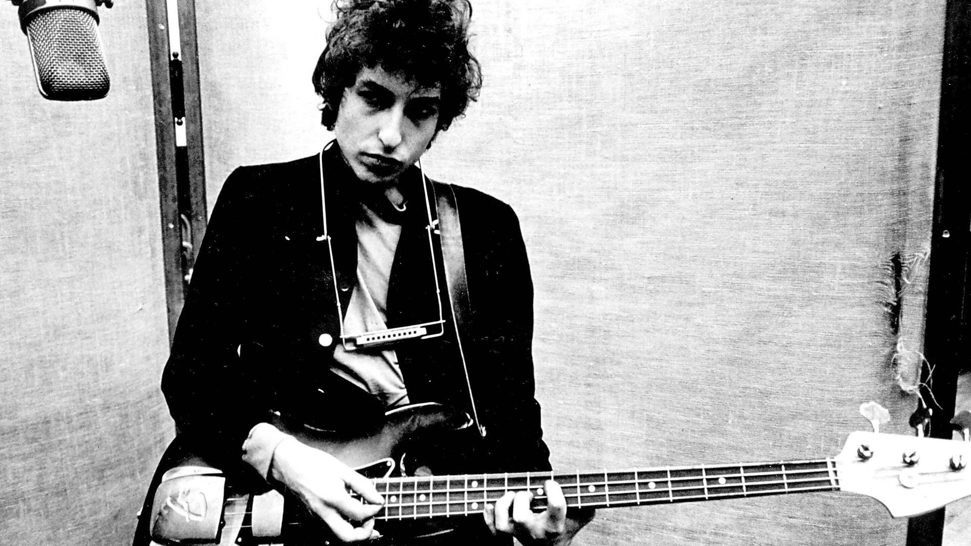 Bob Dylan in einem Studion in New York an einer Fender Jazz Bassgitarre, um seinen Hals hängt eine Mundharmonika. Bob Dylan in einem Studion in New York an einer Fender Jazz Bassgitarre, um seinen Hals hängt eine Mundharmonika.