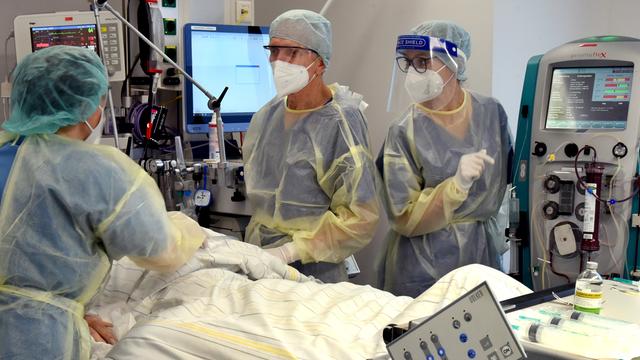 Ärzte und eine Pflegerin stehen um das Bett eines Corona-Patienten auf der Intensivstation. Sie tragen am ganzen Körper Schutzkleidung.