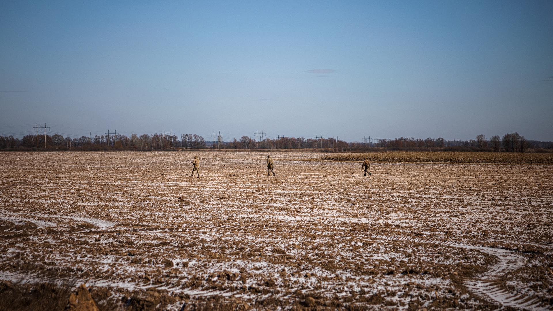 Drei ukrainische Soldaten gehen durch einen Acker, in Bildhintergrund sind weitere landwirtschaftliche Nutzfelder zu erkennen. Drei ukrainische Soldaten gehen durch einen Acker, in Bildhintergrund sind weitere landwirtschaftliche Nutzfelder zu erkennen.