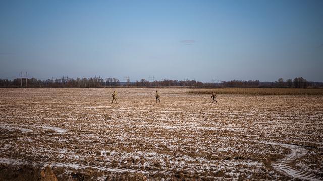Drei ukrainische Soldaten gehen durch einen Acker, in Bildhintergrund sind weitere landwirtschaftliche Nutzfelder zu erkennen.