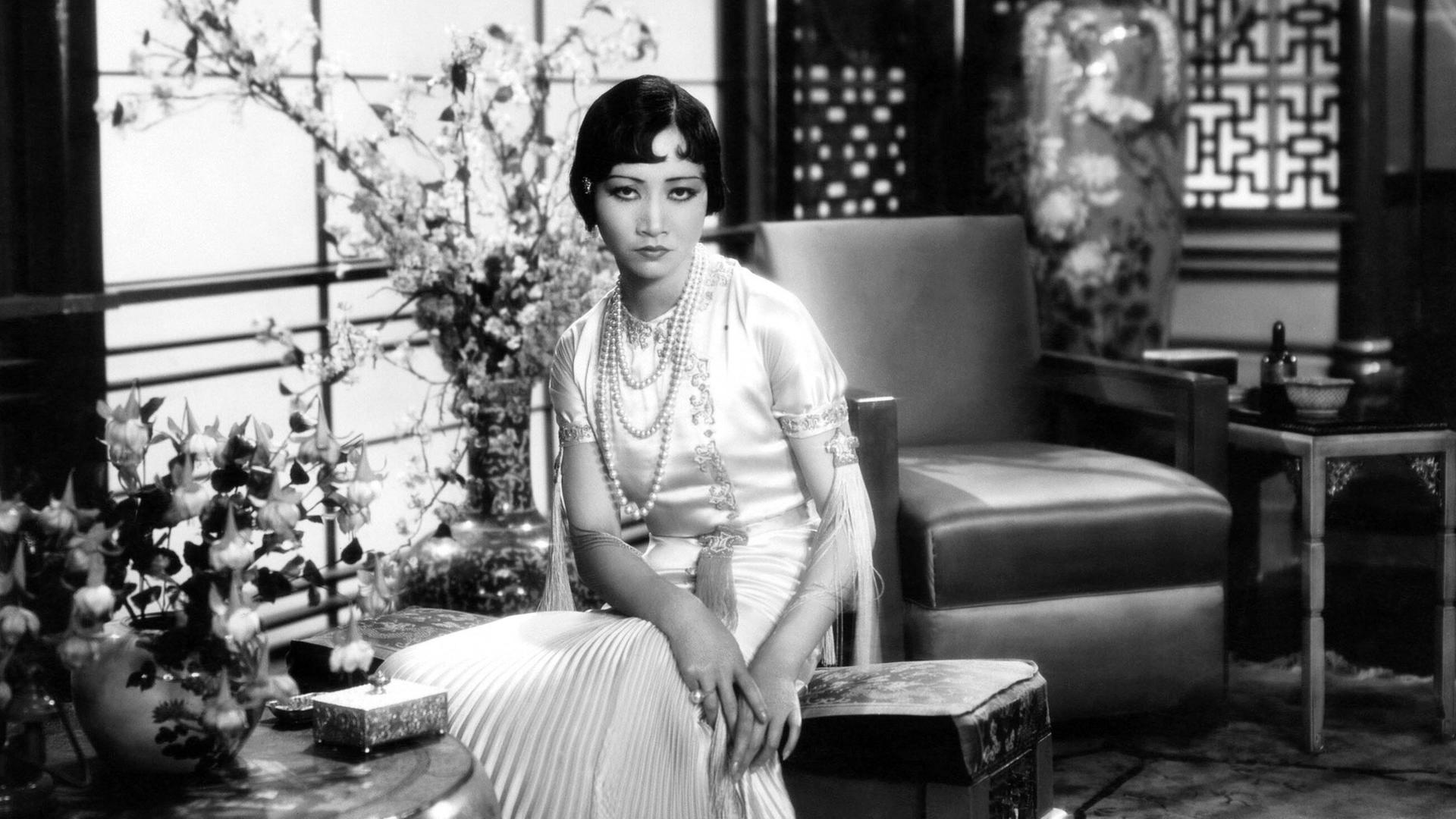 Anna May Wong sitzt in einem großen Salon vor einem Fenster, im Hintergrund Sessel und eine große Vase Anna May Wong sitzt in einem großen Salon vor einem Fenster, im Hintergrund Sessel und eine große Vase