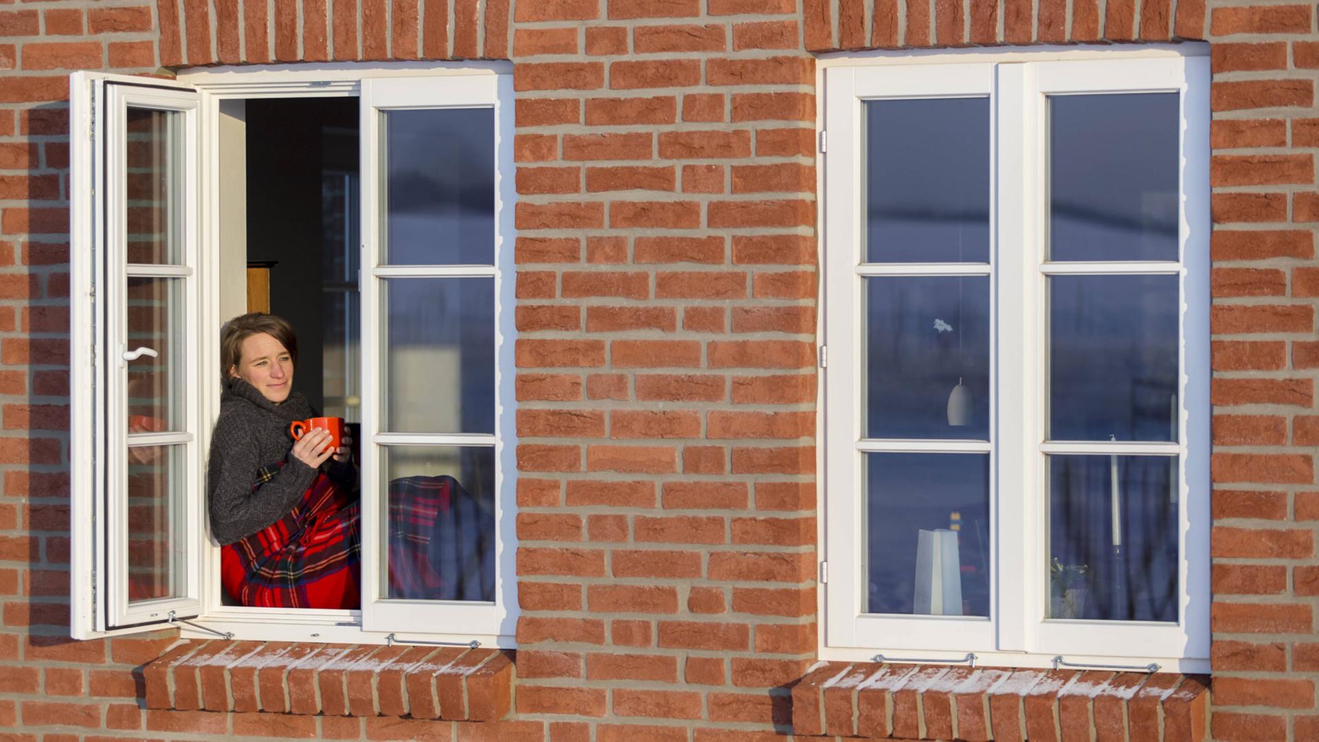 Gemütliches Barnstedt: Junge Frau sitzt auf einem Fensterbrett mit Wolldecke und Kaffeetasse in der Hand Gemütliches Barnstedt: Junge Frau sitzt auf einem Fensterbrett mit Wolldecke und Kaffeetasse in der Hand