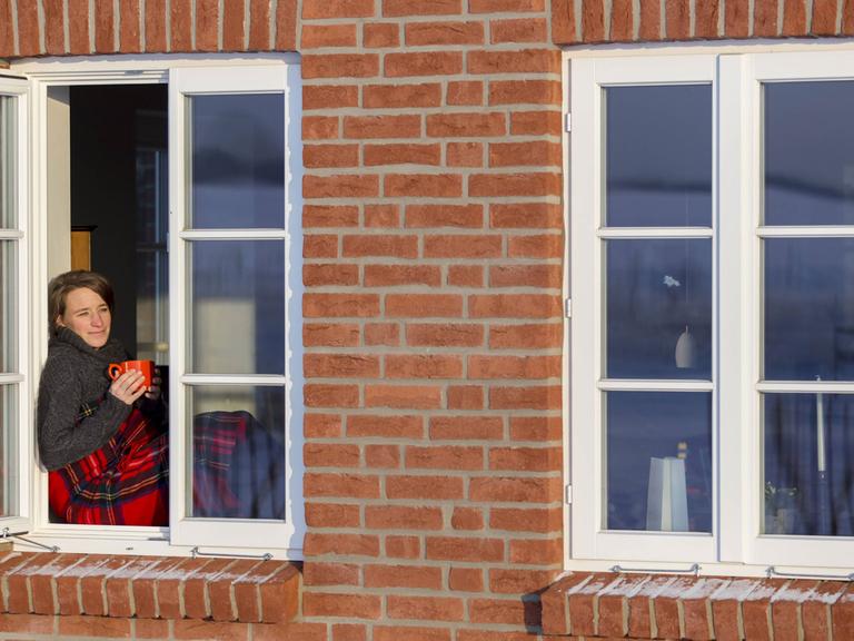 Gemütliches Barnstedt: Junge Frau sitzt auf einem Fensterbrett mit Wolldecke und Kaffeetasse in der Hand