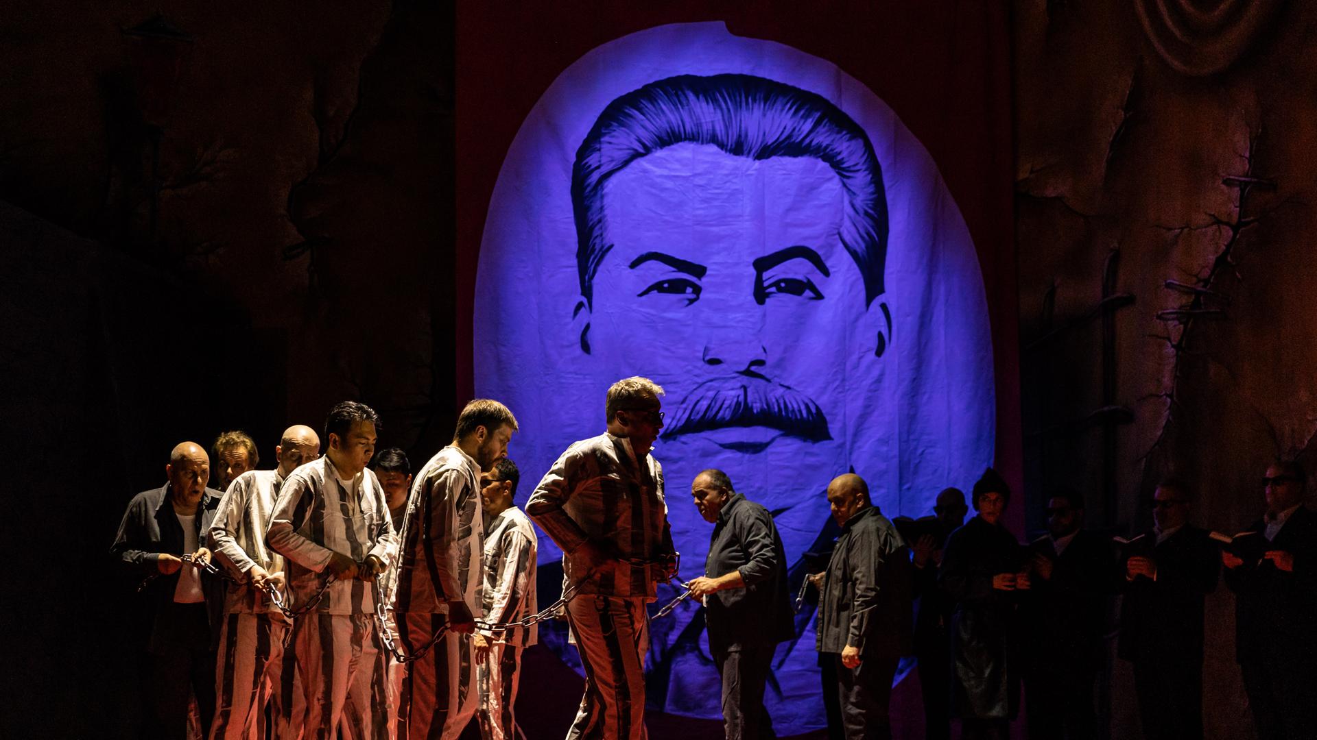 Darsteller in Gefängniskleidung und in Ketten vor einem Porträt von Stalin.