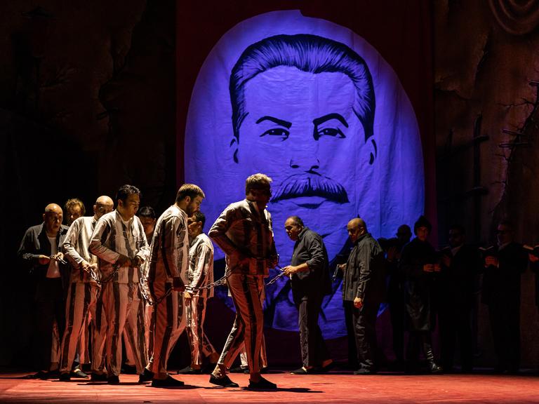 Darsteller in Gefängniskleidung und in Ketten vor einem Porträt von Stalin.