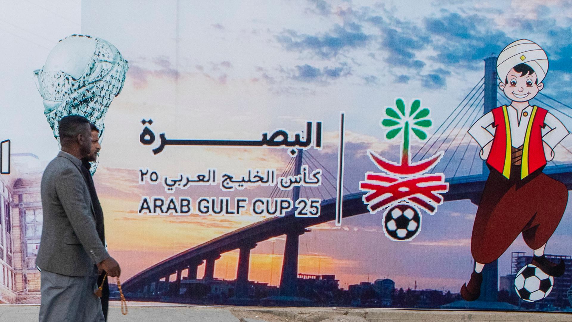Menschen gehen an einer Plakatwand vorbei, die den Arabischen Golfpokal in Basra ankündigt