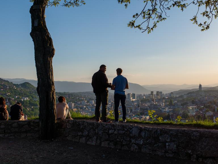 Kemal und Srdjan - die beiden ehemaligen Soldaten sind in etwa gleich alt, stehen auf einer Mauer und blicken auf Sarajewo.