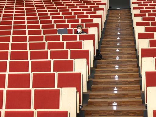 An der Universität Leipzig sitzt ein Informatikstudent bei einer digitalen Vorlesung allein im Auditorium maximum. Er blickt auf seinen Laptop, die Stuhlreihen sind sonst leer.