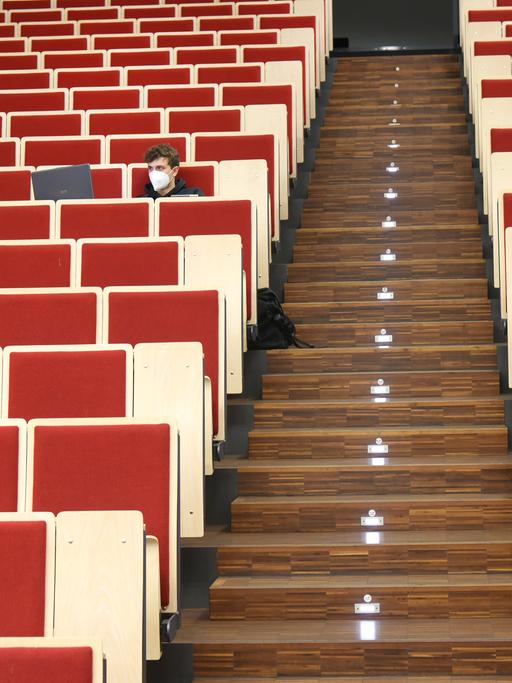 An der Universität Leipzig sitzt ein Informatikstudent bei einer digitalen Vorlesung allein im Auditorium maximum. Er blickt auf seinen Laptop, die Stuhlreihen sind sonst leer.