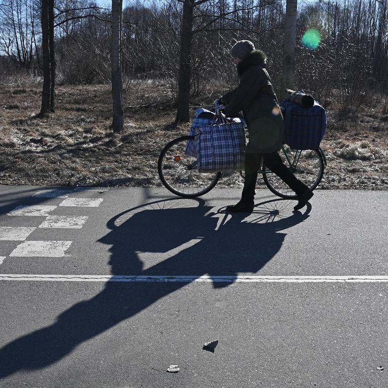 Eine Frau schiebt ein Fahrrad über eine asphaltierte Straße