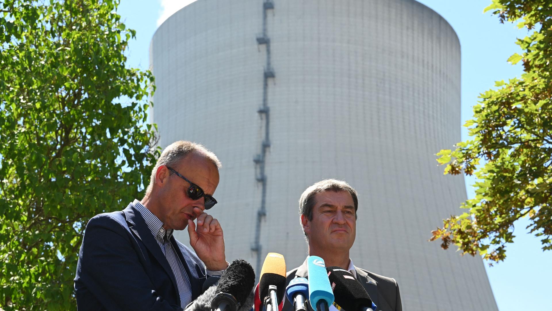 Markus Söder und Friedrich Merz stehen hinter Mikrofonen. Hinter ihnen der Kühlturm des Kernkraftwerks Isar 2. Markus Söder und Friedrich Merz stehen hinter Mikrofonen. Hinter ihnen der Kühlturm des Kernkraftwerks Isar 2.