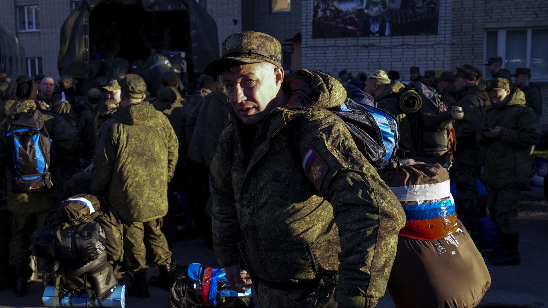 Zu sehen ist ein Mann in Militäruniform mit Schlafsack und Gepäck das mit Tape in den Farben der russischen Flagge zusammengeklebt wurde.
Zu sehen ist ein Mann in Militäruniform mit Schlafsack und Gepäck das mit Tape in den Farben der russischen Flagge zusammengeklebt wurde.
