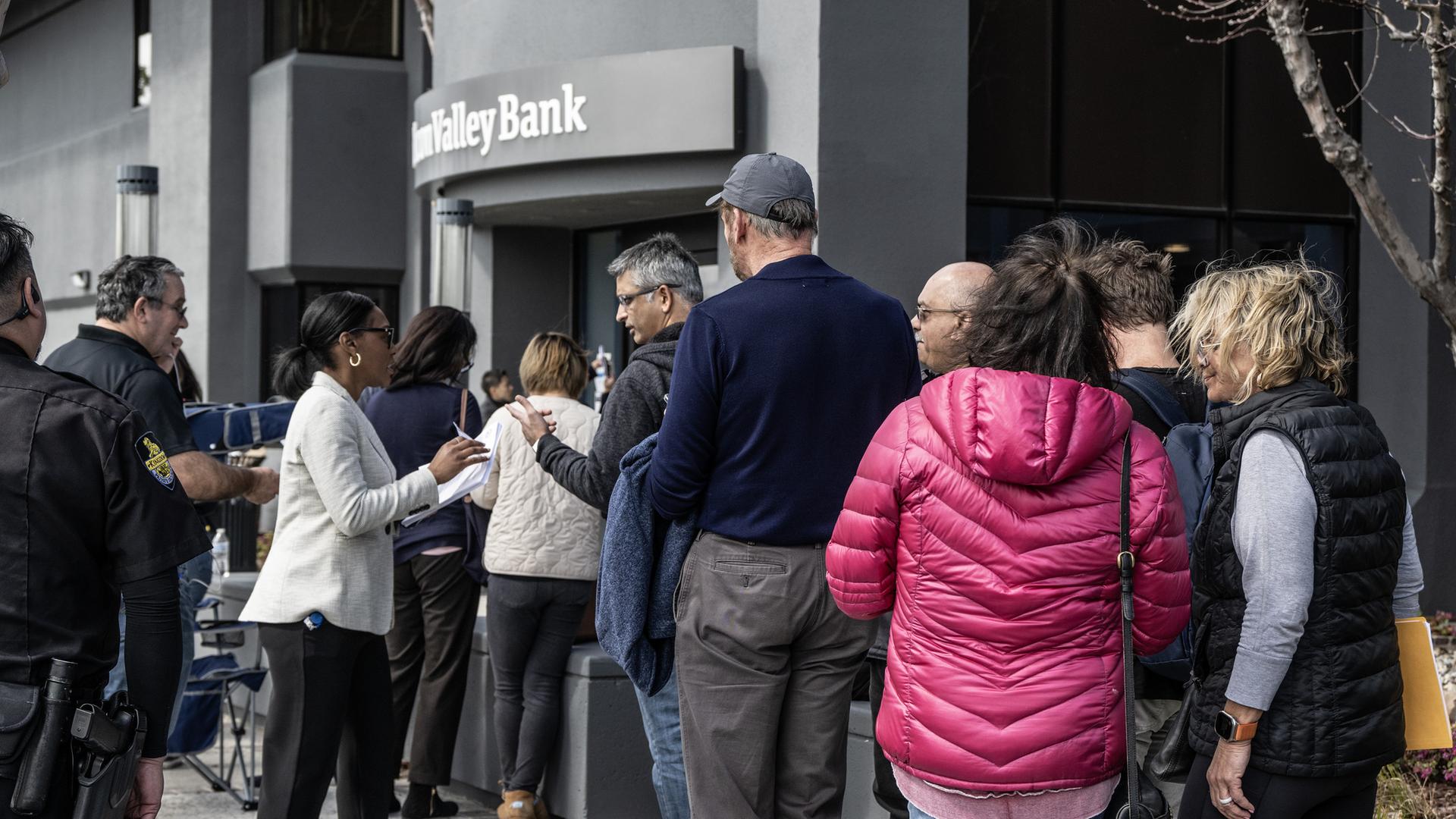 Eine Angestellte der pleite gegangenen Silicon-Valley-Bank in Santa Clara verteilt Papiere an Kundinnen und Kunden der Bank, die am 13. März 2023 vor der Tür auf Einlass warten. Eine Angestellte der pleite gegangenen Silicon-Valley-Bank in Santa Clara verteilt Papiere an Kundinnen und Kunden der Bank, die am 13. März 2023 vor der Tür auf Einlass warten.