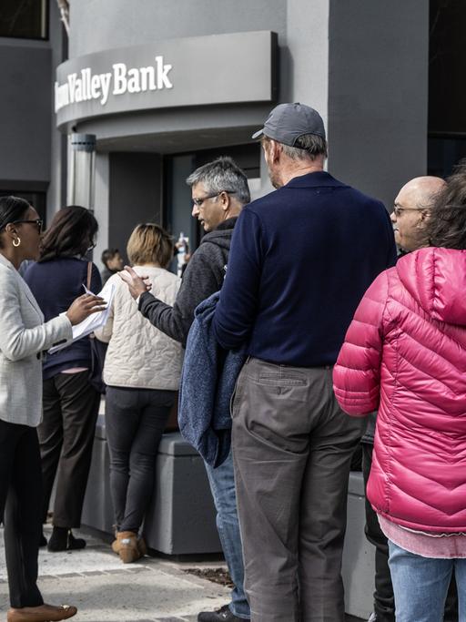 Eine Angestellte der pleite gegangenen Silicon-Valley-Bank in Santa Clara verteilt Papiere an Kundinnen und Kunden der Bank, die am 13. März 2023 vor der Tür auf Einlass warten.