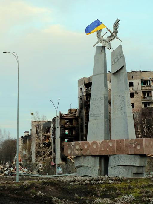 Eine ukranische Flagge weht an einem Denkmal vor bei Angriffen der russischen Armee zerstörten Häusern in der Siedlung Borodjanka bei Kiew 