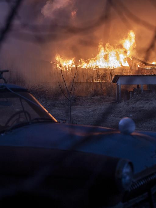 Das Bild zeigt ein brennendes Gebäude, im Vordergrund steht ein Auto