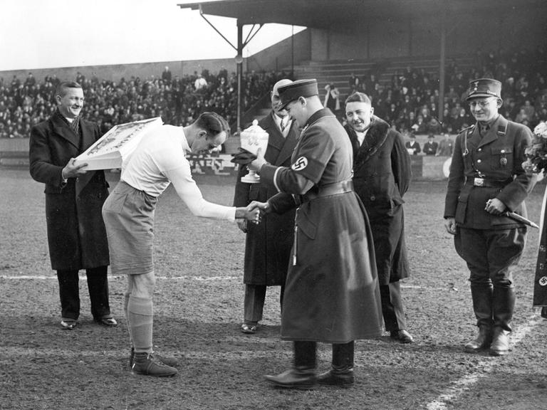 Hanne Sobek von Hertha BSC (links) erhält den Meisterschaftspokal in der Gauliga durch Gauführer Glöckler im März 1935 (vorn rechts) ca. März 1935 in Berlin. Gauliga Berlin-Brandenburg. 