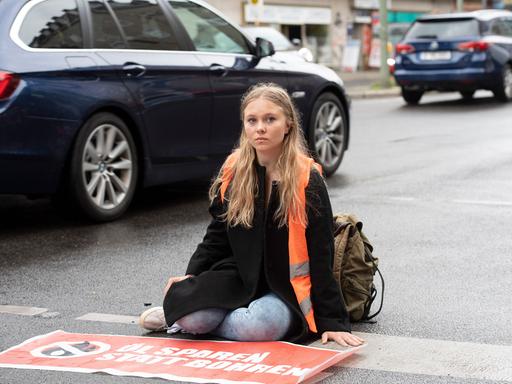 Klebeprotestlerin Aimée van Baalen sitzt festgeklebt auf einer Straße.
