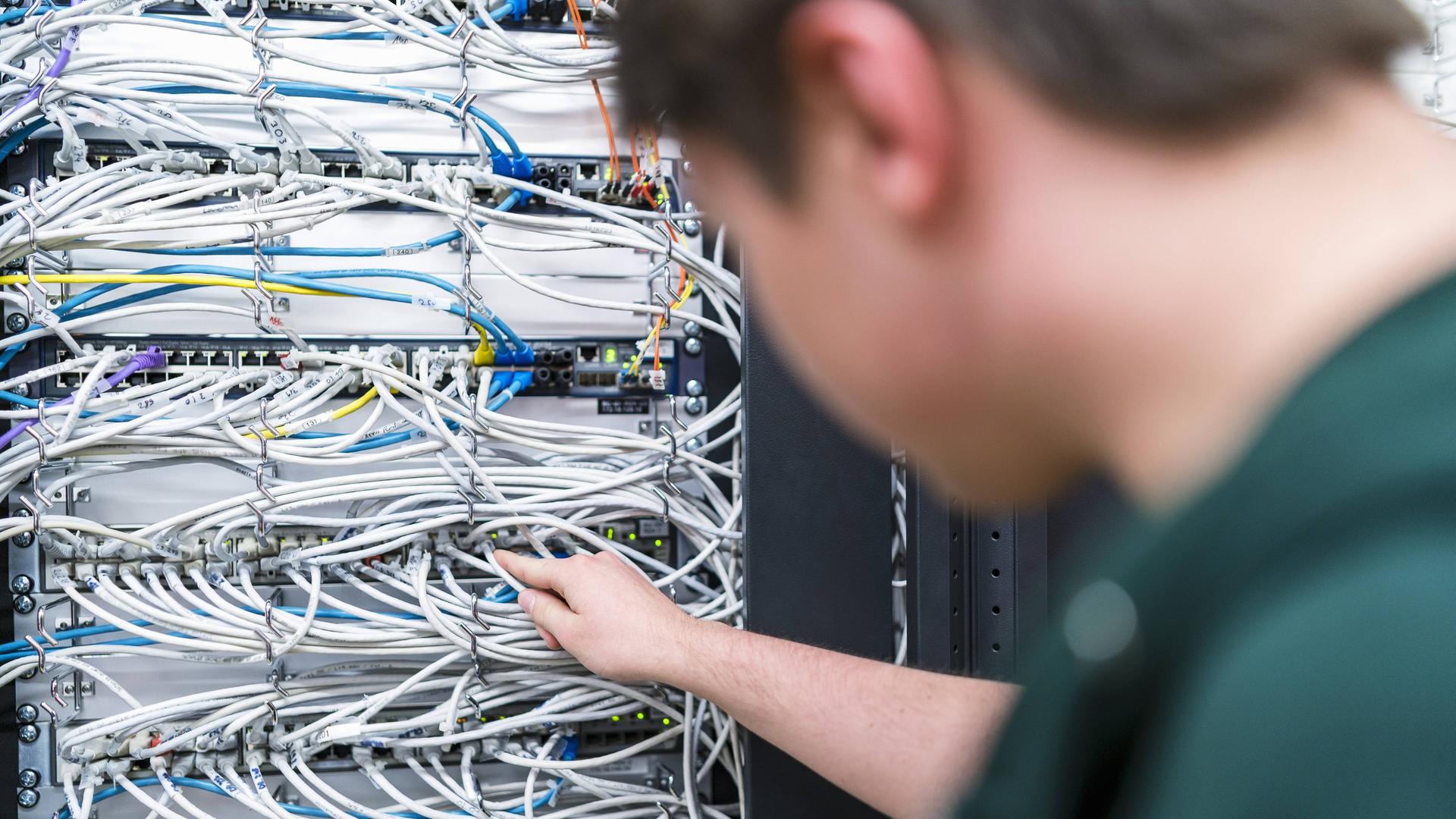 Ein Jugendlicher arbeitet an Kabeln in einem Serverraum Ein Jugendlicher arbeitet an Kabeln in einem Serverraum