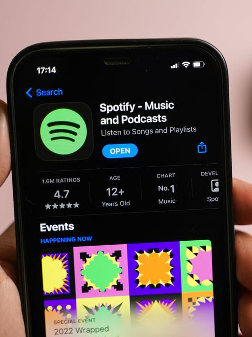 Eine Hand, die ein Smartphone hält, auf ihm ist die Spotify-App geöffnet.