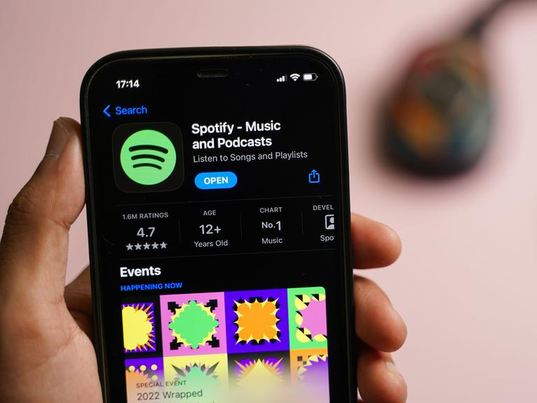 Eine Hand, die ein Smartphone hält, auf ihm ist die Spotify-App geöffnet.