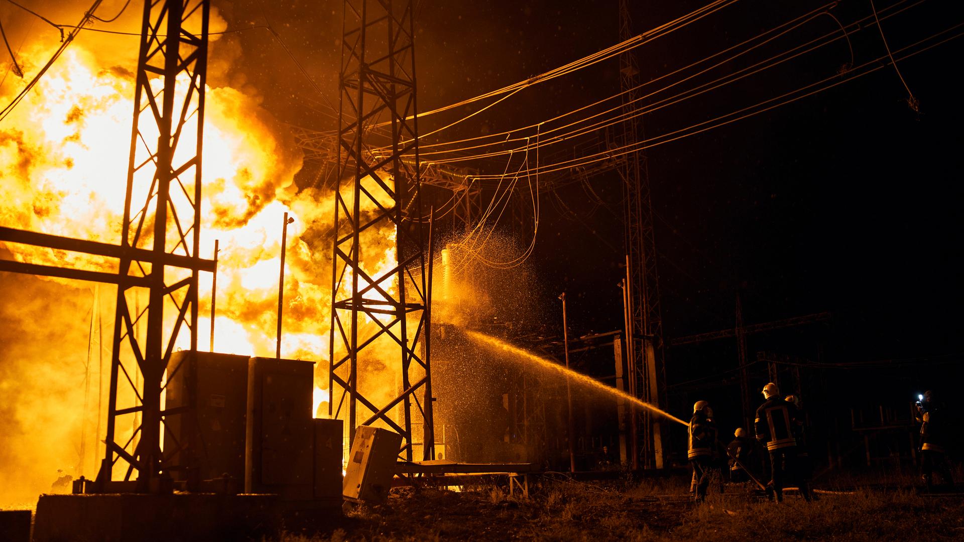 Ein E-Werk brennt. Ukrainische Feuerwehrleute versuchen nachts, die Flammen zu lösche.