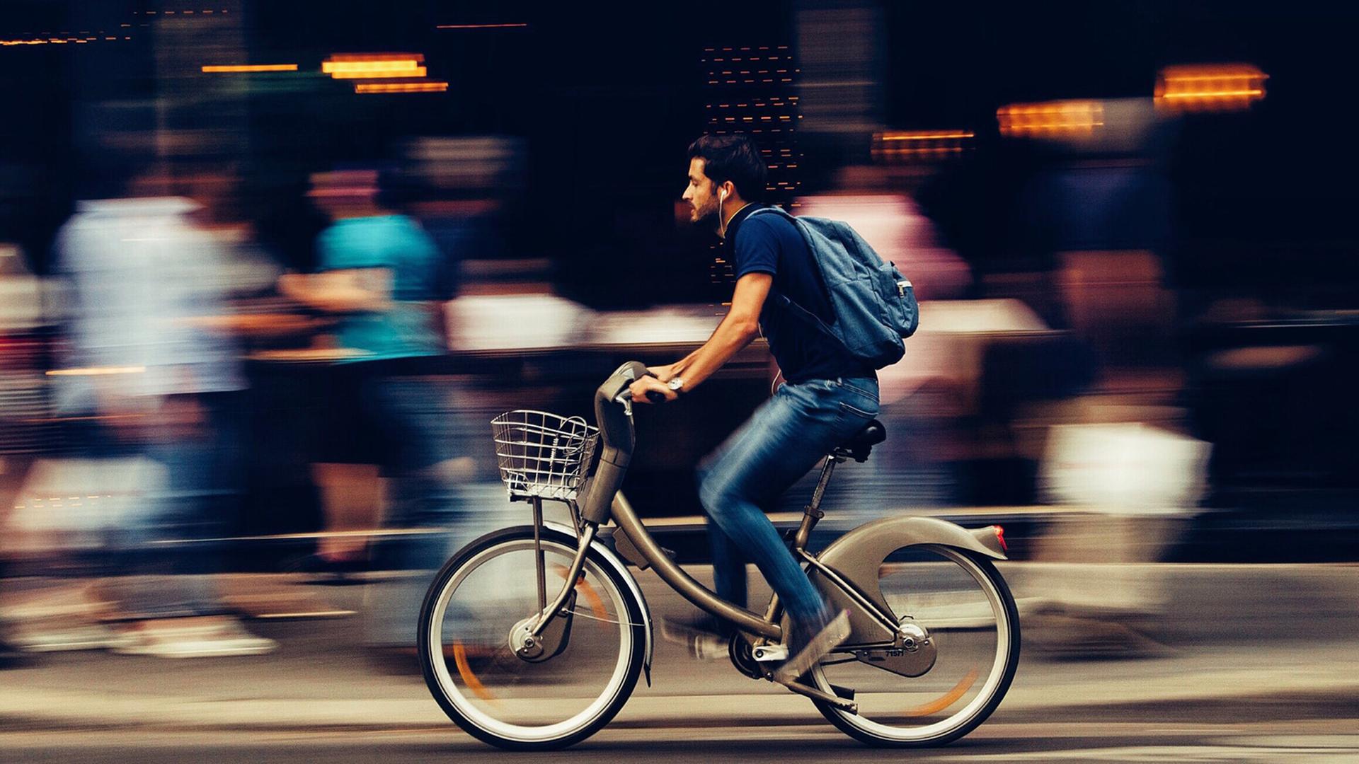 Ein junger Mann auf einem Fahrrad fährt schnell eine belebte Straße entlang. 