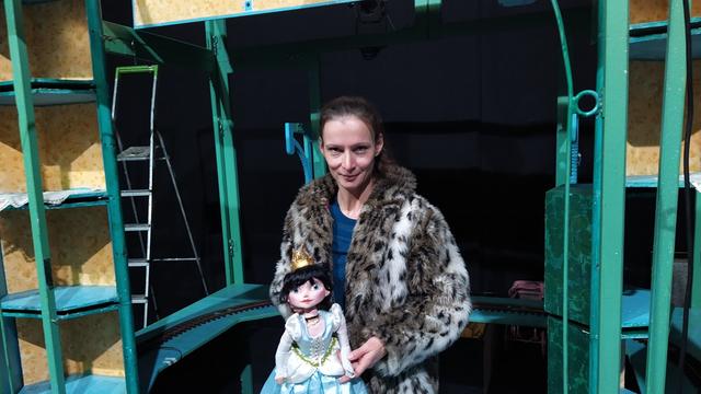 Die Schauspielerin Nicole Gospodarek steht in einem Puppentheater und hält eine Puppe vor sich. Sie lächelt dabei in die Kamera.