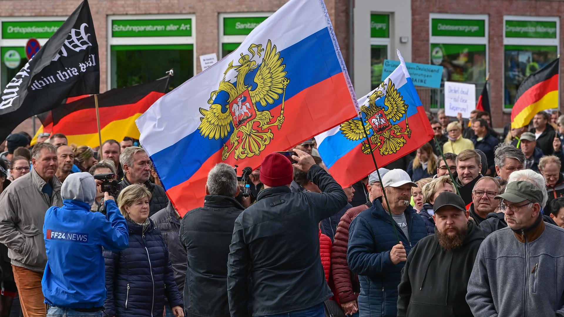 Viele Menschen nehmen an einer Protest-Demonstration teil und schwenken dabei unter anderem auch Russland-Fahnen und die deutsche Fahne. 