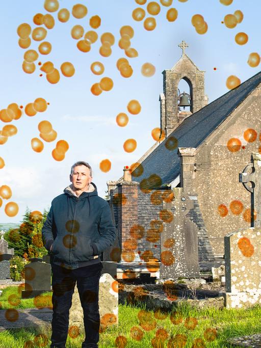 Ein Mann steht auf einem Friedhof und schaut in die Kamera.